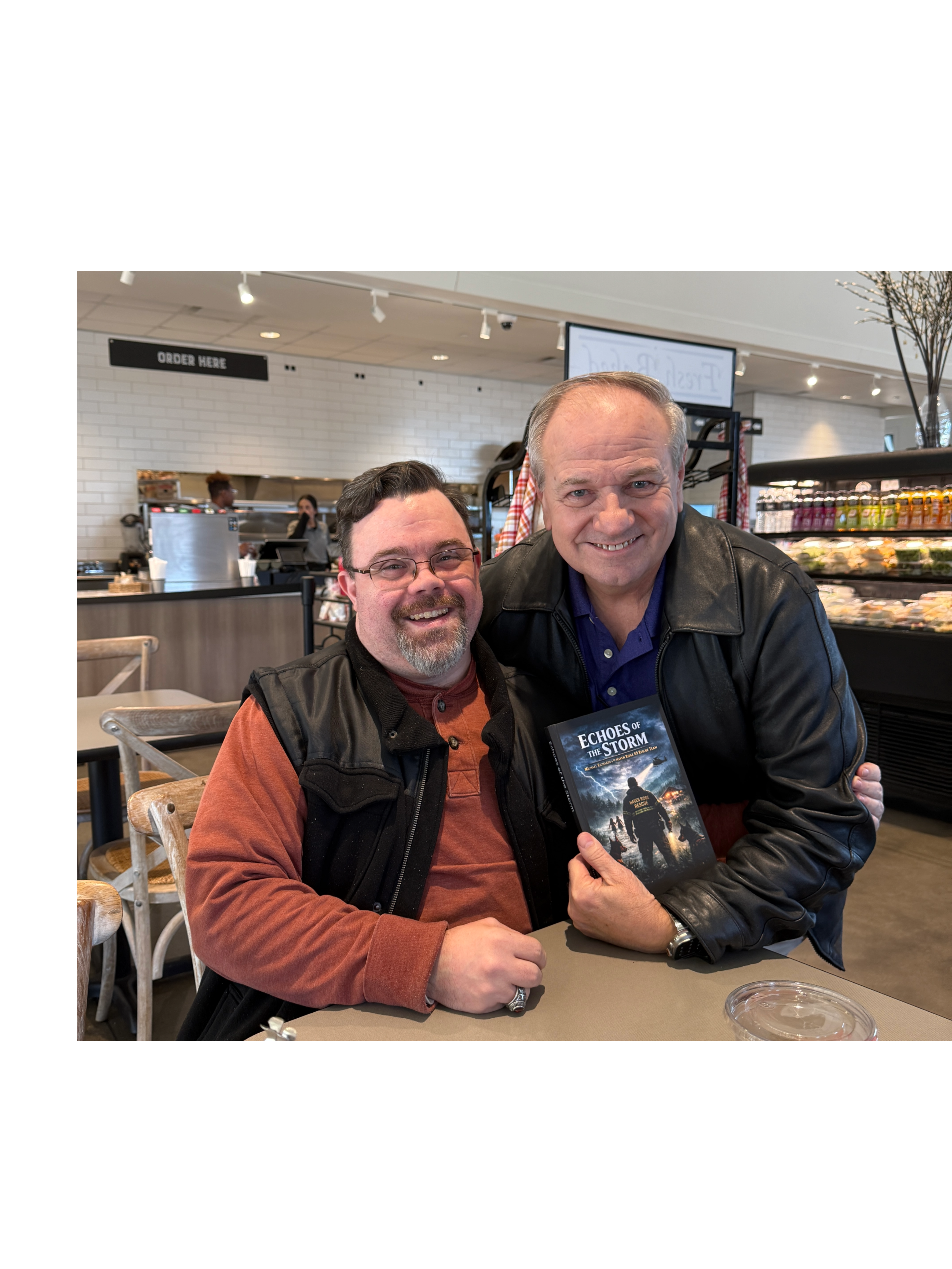Stacy Richards with a reader holding a copy of Echoes of the Storm at a café signing